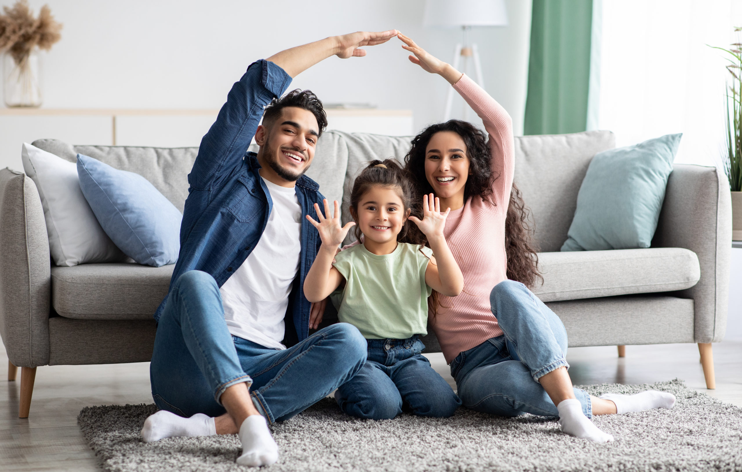 Family care. Arabic parents making symbolic roof of hands above cute little daughter while sitting together on floor in living room, middle eastern mom and dad having fun with their child at home